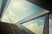 A stairway leading up to blue sky with sun over light cloud