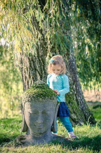 Little girl and a Buddha head in a zen garden