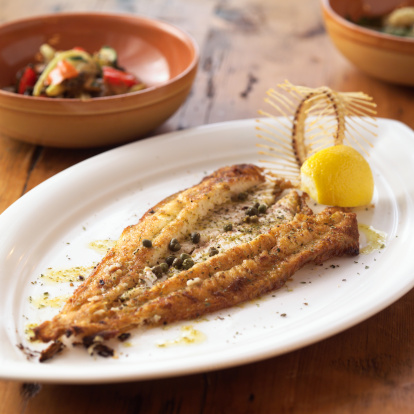 Filet of dover sole with capers, lemon and bone as garnish.  Shot with very shallow focus.