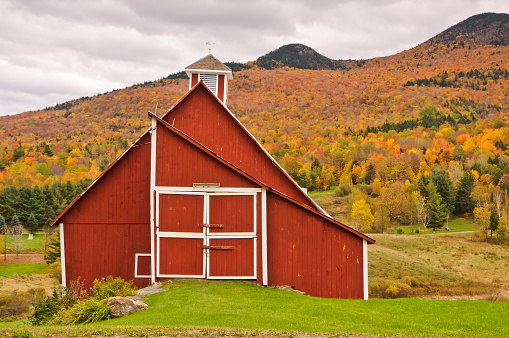An old red barn along a backroad near Stowe, Vermont with a backdrop of autumn foliage.