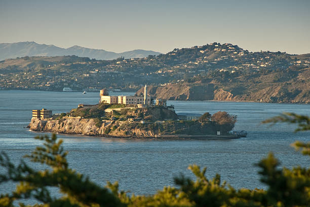Alcatraz Island at Sunset Between 1934 and 1963, the 22 acres of Alcatraz Island contained a lighthouse, a military fortification, a military prison, and a federal prison. Today, the island and its facilities are managed by the National Park Service as part of the Golden Gate National Recreation Area. In 1986, Alcatraz received designation as a National Historic Landmark. Alcatraz Island is in San Francisco Bay, 1.25 miles offshore from San Francisco, California, USA. jeff goulden government building stock pictures, royalty-free photos & images
