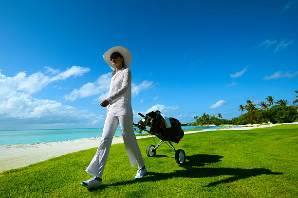 femme de golf avec voiturette marchant sur la plage sur le parcours de golf - fitness trainer photos et images de collection