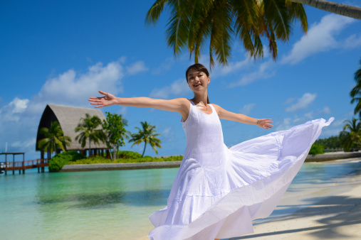 a happy asian young woman is dancing and turning her skirt on beach