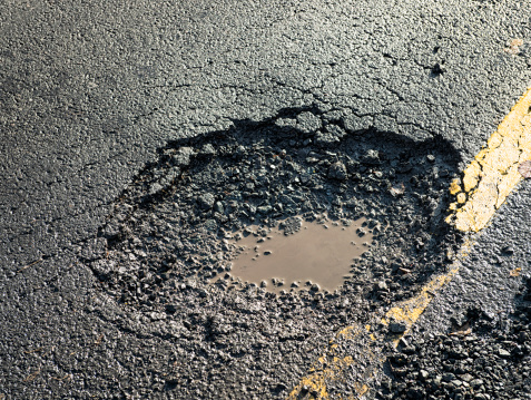 Close-up of the effects of road weathering and neglect - a deep pot hole causing a danger to drivers.