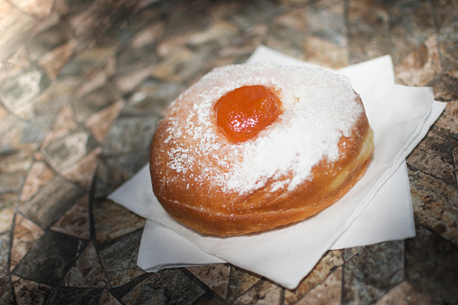 Traditional donut with apricot jam and sugar powder on napkins on the table.