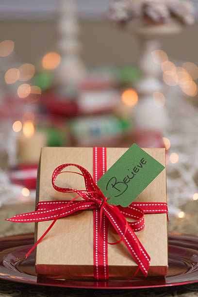 Vertical photo of gift in gold box with red ribbon at a table set for the holidays. Green tag with word \