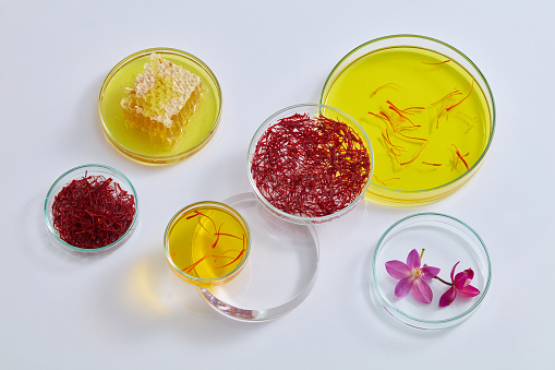 Honeycomb, saffron, flowers and liquid contained inside many petri dishes in different sizes. Saffron is a spice with a strong fragrance and distinctive color