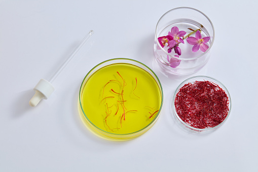 Purple flowers put inside a glass jar arranged with petri dishes of yellow liquid and saffron. A dropper featured. Saffron benefits your health in numerous ways