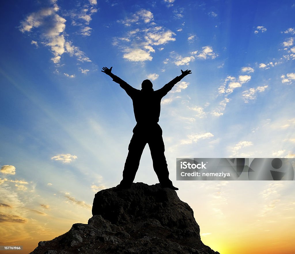 Silhouette of a man standing on top of the mountain Silhouette of man and sunshine on sky background. Achievement Stock Photo