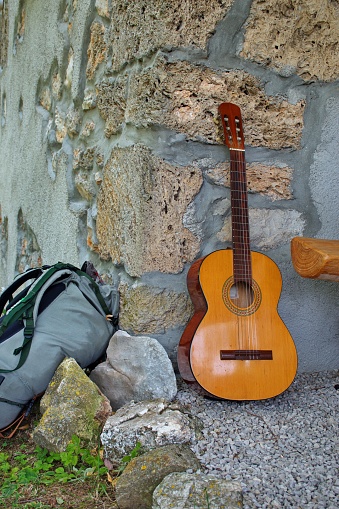 Acoustic guitar and backpack leaning against a stone wall