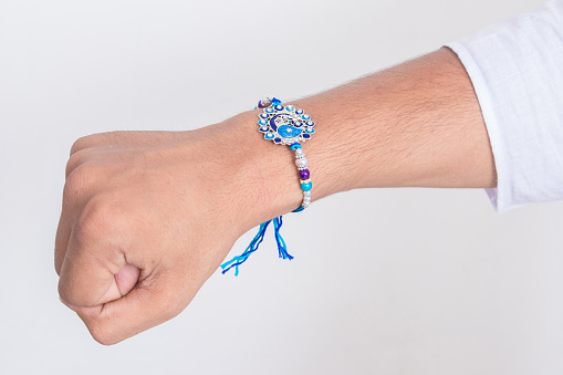Hand wearing beautiful blue diamond design rakhi on the occasion of raksha bandhan over white background. Indian festival celebrated in India to express love and bond between brother and sister.