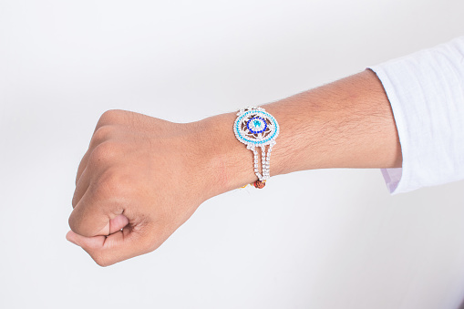 Hand wearing beautiful blue diamond design rakhi on the occasion of raksha bandhan over white background. Indian festival celebrated in India to express love and bond between brother and sister.