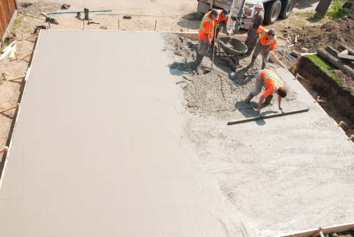 Crew of concrete workers pouring and leveling a garage pad. Half of the pad is done and would make great copy space.