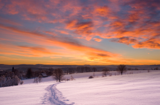 Mist on the ground over a snow-covered hillside landscape on the Mangfall valley in Upper Bavaria at dusk, Germany