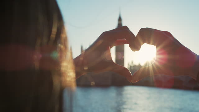 Close up of attractive woman hands making heart shape gesture at sunset in front of Big Ben palace of westminster