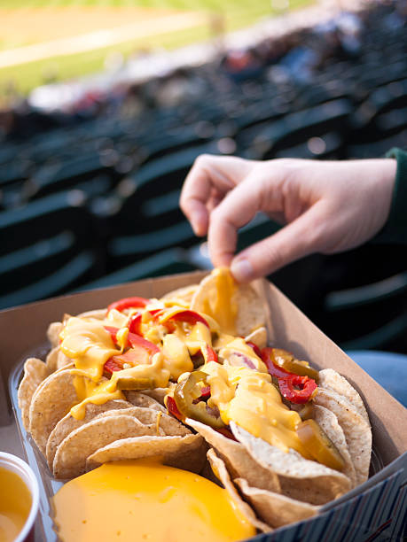 Eating Nachos at a Baseball Game Ballpark Sports Stadium A person's hand picking up nacho chips at a baseball ballpark. baseball stadium chairs stock pictures, royalty-free photos & images