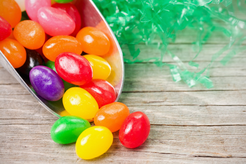 A scoop of colorful jellybeans with decorative artificial grass on an old, weathered wood surface.