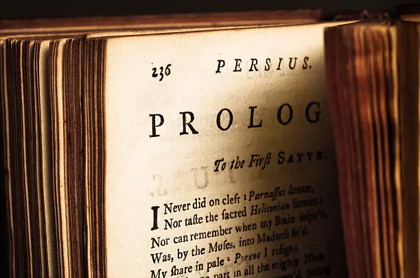 Opened antique edition (printed in London 1735) of The Satyrs of Decimus Junius Juvenalis and Aulus Persius Flaccus, both Roman poets, translated into English by John Dryden. This is the Prologue page from Persius Satyrs. Warm side-lighting with intentional deep shadows.