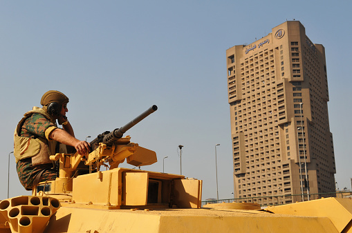 a man with a UAV control panel in his hands, a drone flying above the tank in the background in nature. help of reconnaissance drones in modern warfare.