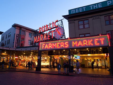 Seattle, USA - Jun 26, 2020: The famous neon Public Market Center sign at Pike Place Market at sunset with LGBT flags.