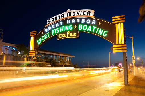 Santa Monica, USA - March, 12 2010: Santa Monica Pier neon sign entrance leading to the Pacific Park, a family amusement park with a large Ferris wheel.