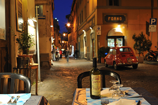 Rome, Italy, November 30 -- A lonely adult man sitting in the evening in a typical restaurant and wine bar along Via del Banco di Santo Spirito, in the Rione Ponte, in the historic heart of Rome. In the background the famous Castel Sant'Angelo. In 1980 the historic center of Rome was declared a World Heritage Site by Unesco. Image in high definition quality.