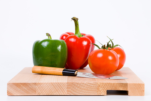 Hands cutting red bell peppers on a wooden chopping board. Woman chopping bell peppers in kitchen close up.