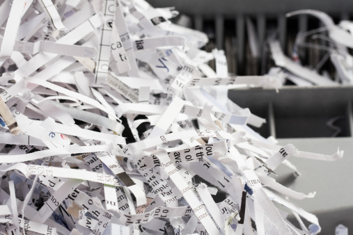 Close up image of a pile of shredded paper documents in front of a paper shredder.