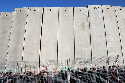 Palestinians wait in line at the tall concrete wall separating Bethlehem and Jerusalem, waiting to cross through an Israeli security checkpoint.