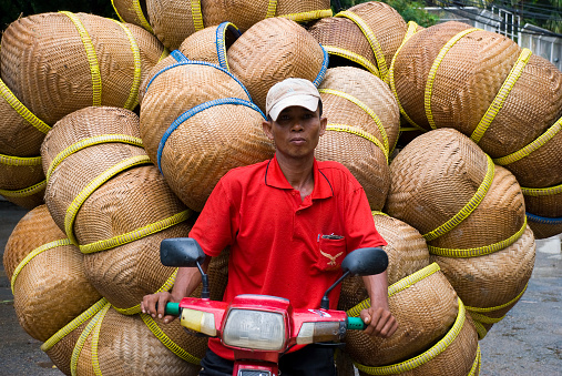 A Cambodian man drives a motorcycle with a large cargo of woven baskets in Phnom Penh, Cambodia