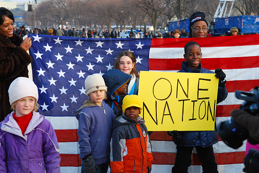 White and black children stand with the American flag and a sign that reads 