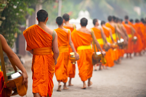 Two young Asian monk stay with other monk on green big buddha statue to clean in area of body of statue with warm light of early morning.