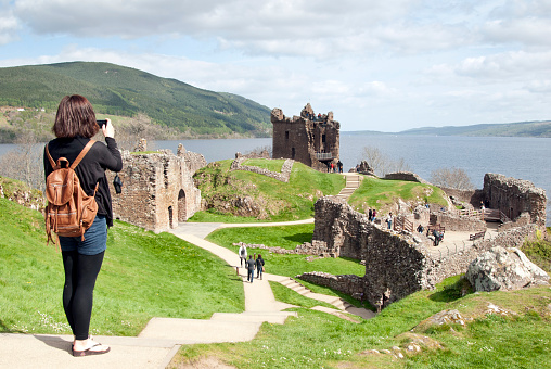 Urquhart, Scotland - April 25, 2011: Young women taking a picture of the ruins of Urquhart Castle which sits on the banks of Loch Ness. The ruins of Urquhart Castle which sits on the banks of Loch Ness, has been voted one of Britain's favourite tourist spots, on September 11, 2008 in Urquhart, Scotland. The poll commissioned by the RAC, put forward a shortlist of 14 places, compiled by Visit Britain.