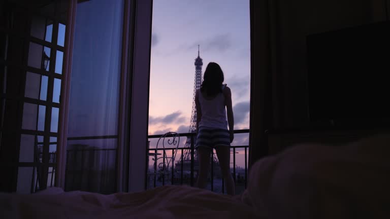 Young tourist woman stretching at sunrise on hotel terrace with view of Eiffel Tower Paris arms raised enjoying european travel adventure celebrating beautiful city