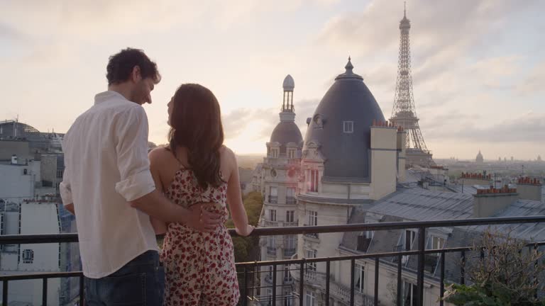 Romantic couple looking out over Paris view from Hotel balcony terrace Eiffel Tower in background at sunrise