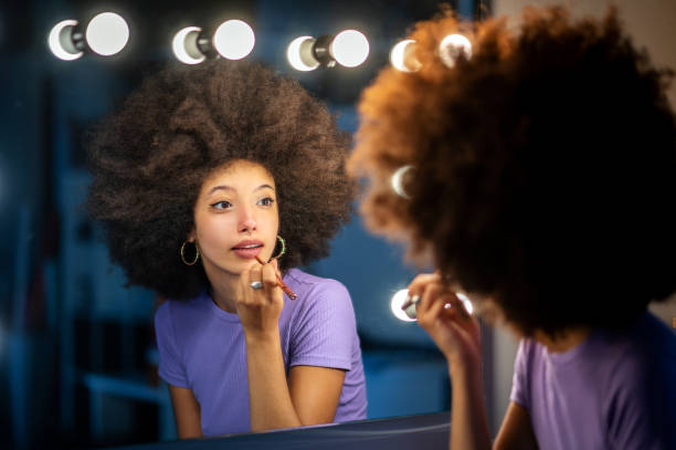 Woman with Afro hairstyle applying makeup against mirror