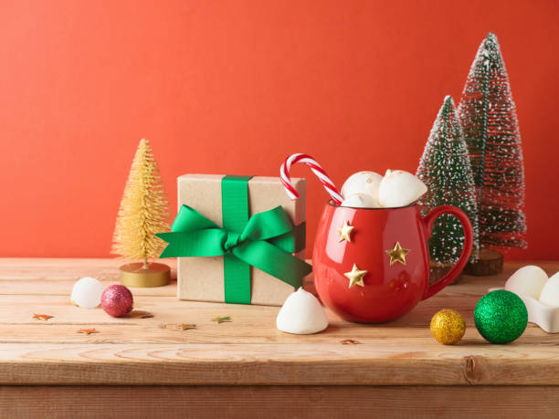 istock Christmas hot chocolate cup with marshmallow, gift box and decorations on wooden table over red background 1577875242
