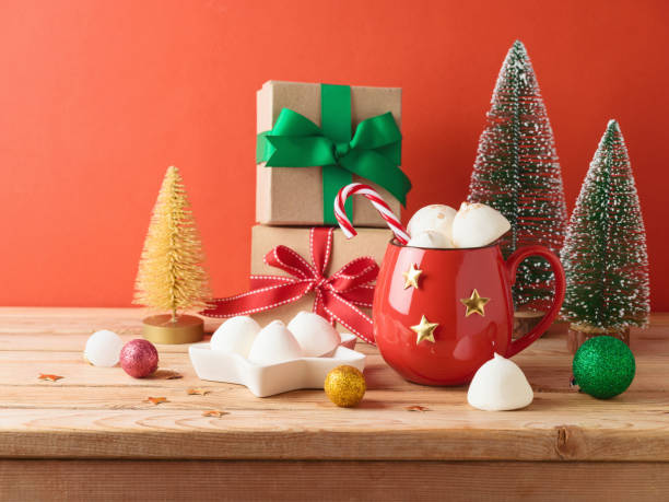 istock Christmas hot chocolate cup with marshmallow, gift box and decorations on wooden table over red background 1577875246