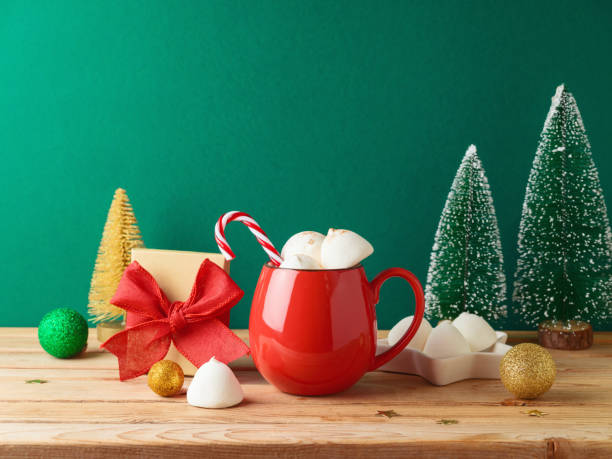 istock Christmas hot chocolate cup with marshmallow, gift box and decorations on wooden table over green background. Festive greeting card 1577875247