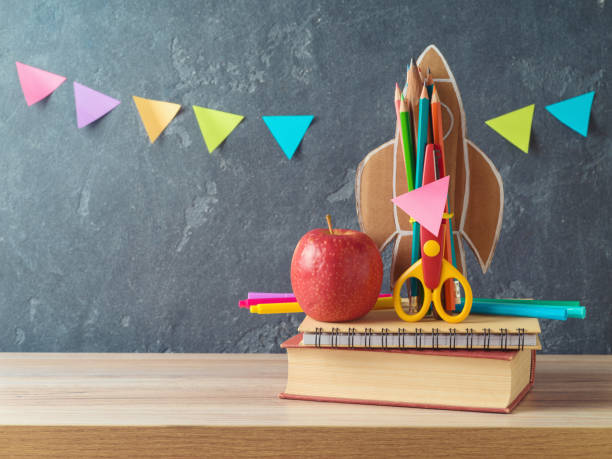 istock Back to school concept with rocket, pencils, apple and book on wooden table over blackboard background 1577875769