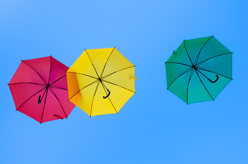 Three colorful umbrellas - red, yellow and green - fly in the blue sky