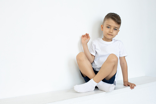 Portrait of a little boy on a white background. The child is wearing a white T-shirt and dark blue shorts.