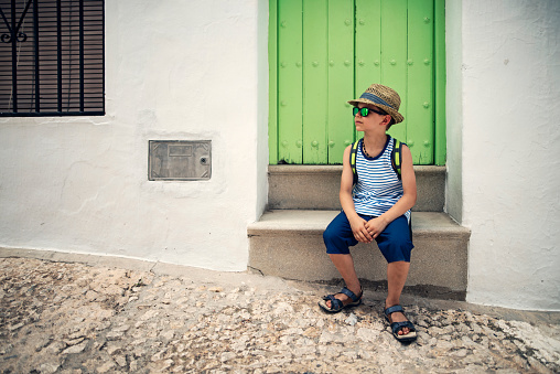 Little boy sightseeing a town in Andalusia, Spain\nThe boy is sitting in front of green door and resting.\nShot with Nikon D810