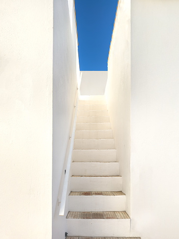 A set of stairs with white walls looking up to a bright blue sky