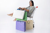 Woman rides in a shopping cart and enjoys sales. Successful shopping and consumerism. Studio photography.