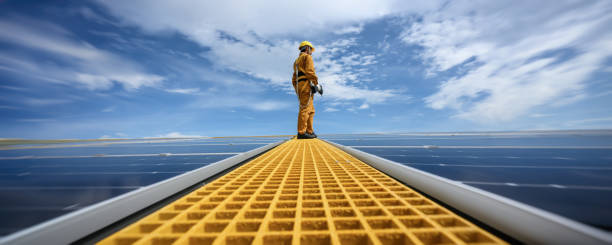 Technician Young Wearing Safety Protective Clothing on Walkway with Tool Standing to Checking Quality of Solar Panel or Photovoltaic Installation in Daytime on Factory Roof Buildings. stock photo