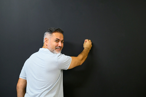 Happy smiling instructor writing on the blackboard in a classroom