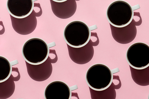 Pattern made of cup of black coffee on pink background