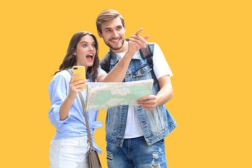 Beautiful young couple holding a map and smiling while standing on yellow background