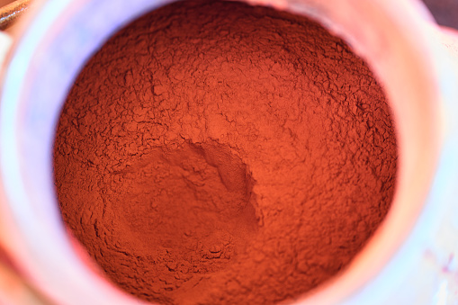 Bright red dry copper electrolytic powder in white bowl on table in metalwork plant workshop extreme close view from above